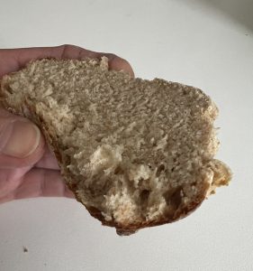 Halbes Brötchen in einer Hand, bereit zum Reinbeißen. Weißer Hintergrund.