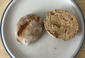 Aufgeschnittenes Brötchen einmal von innen, einmal von außen auf einem weißen, blaurandigen Teller auf Holztisch. 